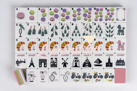 Colorful Mahjong tile set featuring macaroons, champagne, and croissants on white ceramic.