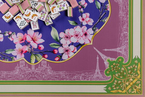 Colorful Mahjong tiles atop a floral patterned mat featuring cherry blossoms and Parisian landmarks.
