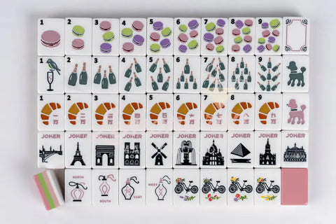 Colorful Mahjong tile set featuring macaroons, champagne, and croissants on white ceramic.