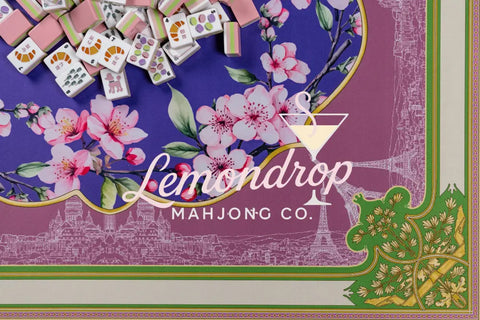 Colorful Mahjong tiles atop a floral patterned mat featuring cherry blossoms and Parisian landmarks.